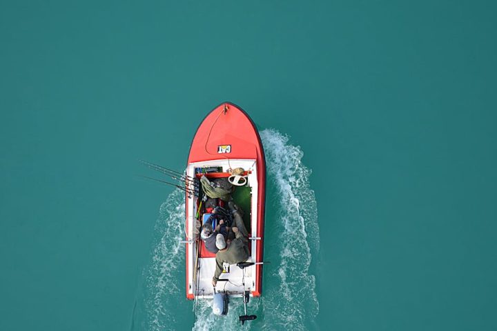 Top view of a red motorboat with fishermen navigating open turquoise waters.